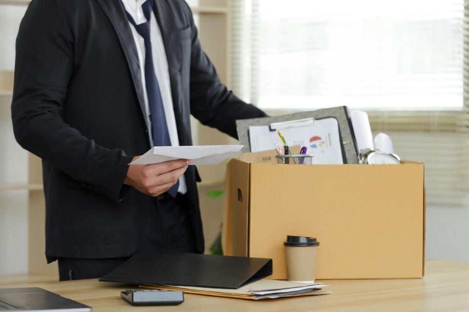 Resignation. The businessman puts his box of his belongs on the desk and holds the white letter. Quitting a job; a businessman fired or leave a job concept. The great Resignation.