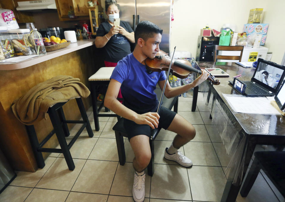 Emilian Sosa, 14, plays the violin for his mother seen through a zoom monitor screen at her hospital bed on Wednesday, Jan. 27, 2021 in McAllen, Texas. The McAllen teen has pleaded to the governor for life-saving COVID treatment for his mom. (Delcia Lopez/The Monitor via AP)