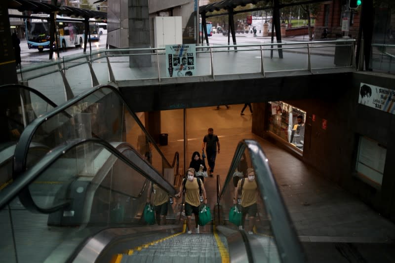 People wearing face masks use escalator at a city transit hub, as New South Wales begins shutting down non-essential businesses and moving toward harsh penalties to enforce self-isolation to avoid the spread of coronavirus disease (COVID-19), in Sydney