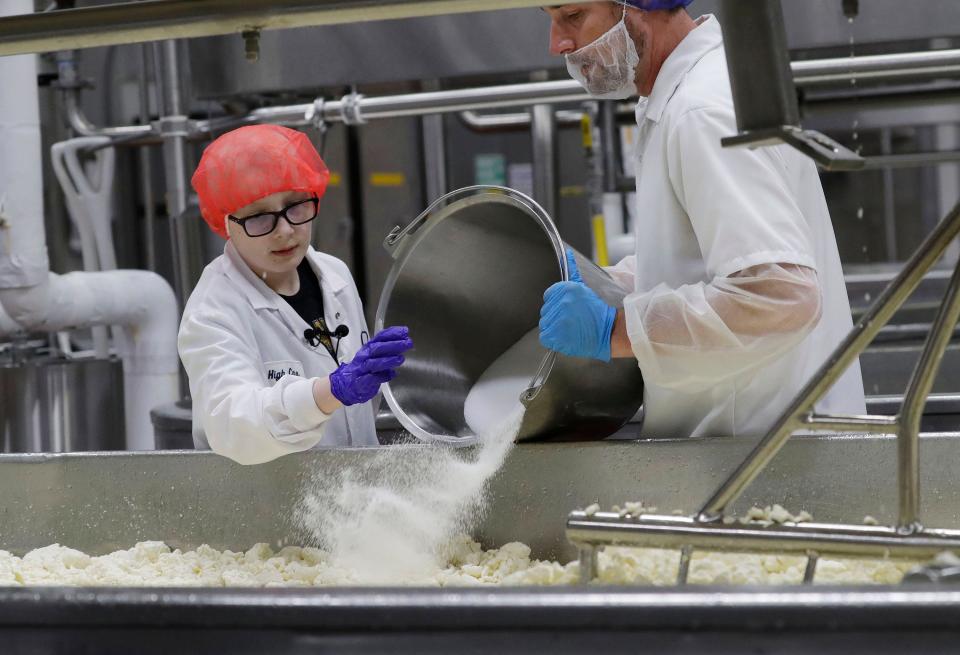 Maxx Ball, 10, of Winston-Salem, North Carolina, pours salt on cheese curds under the supervision of a Sargento Baker Cheese facility employee, Tuesday, November 22, 2022, in St. Cloud, Wis. Ball, who has beaten a form of bone cancer got his chance to see string cheese being made at the plant through Make-A-Wish.