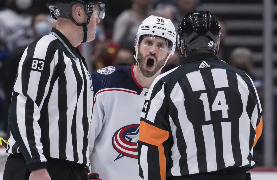 Columbus Blue Jackets' Boone Jenner, back, protests to referee Trevor Hanson, right, after a penalty was called against Andrew Peeke during the third period of an NHL hockey game Tuesday, Dec. 14, 2021 in Vancouver, British Columbia. (Darryl Dyck/The Canadian Press via AP)