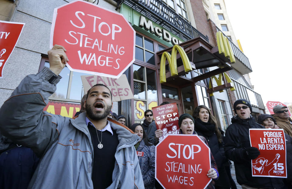 Demonstrator Zev Nicholson, of Boston, left, holds a placard and chants during a protest outside a McDonalds fast foot restaurant, Tuesday, March 18, 2014, in Boston, held to call attention to the denial of overtime pay and other violations protesters say deprive workers of the money they're owed. (AP Photo/Steven Senne)