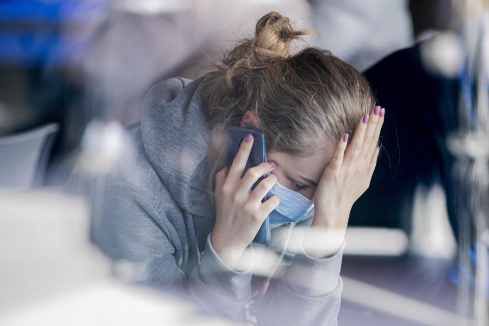 Maja, second name not given, is sitting at Tegel Airport wearing a breathing mask and use her phone as she waits for a bus to leave for Poland in Berlin, Germany, Monday, March 16, 2020. She says that it is no longer possible to return to Poland by plane. For most people, the new coronavirus causes only mild or moderate symptoms, such as fever and cough. For some, especially older adults and people with existing health problems, it can cause more severe illness, including pneumonia. (Christoph Soeder/dpa via AP)