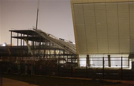 Workers look at the Arena Sao Paulo stadium, known as "Arena Corinthians" and "Itaquerao", in Sao Paulo March 29, 2014. Another man has died while helping to build the stadium that will host the opening match at this year's World Cup in Brazil, a hospital spokesperson said on Saturday. He is the third construction worker to perish while working on the Arena Corinthians on the outskirts of Sao Paulo and the seventh to die in Brazil's World Cup arenas. REUTERS/Nacho Doce