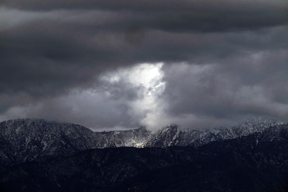 Heavy clouds move over the San Gabriel Mountains range in this view from Los Angeles, Thursday, Feb. 8, 2024. Snow-capped mountains sparkled under brilliant sunshine that replaced days of extreme wet weather that marked a major turnabout from a very slow start to winter. (AP Photo/Damian Dovarganes)