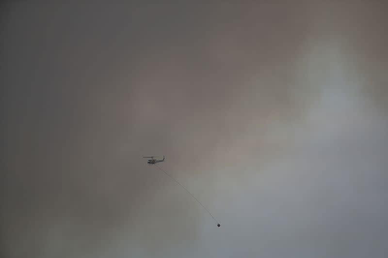 A helicopter carrying out aerial firefighting operations flies through the smoke of a bushfire in Bredbo