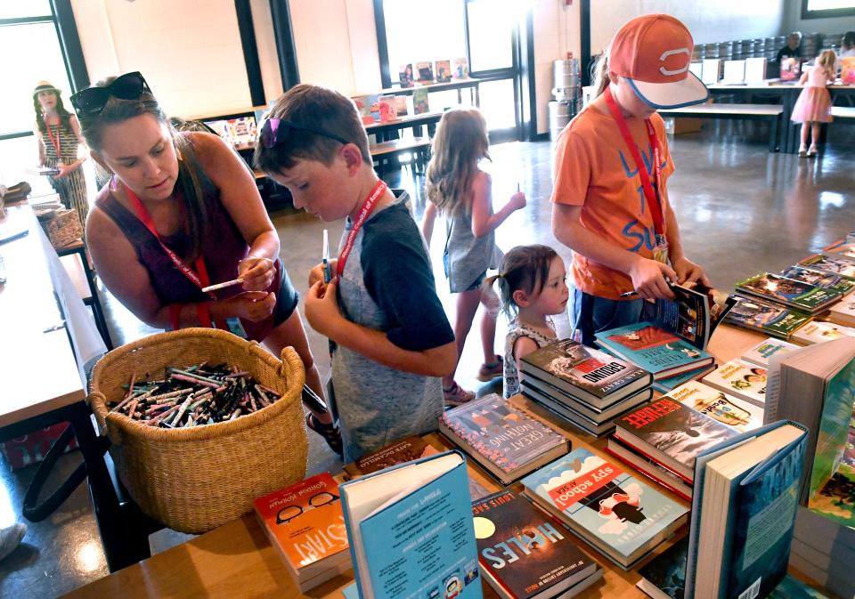 Rochelle White of Merkel (left) helps her son Tucker, 10, pick a pen while her other children browse the selections at Arlene Kasselman's pop-up bookstore Friday. Kasselman's event was in a back room at Grain Theory during the Children's Art & Literacy Festival. She will open a permanent location this summer downtown