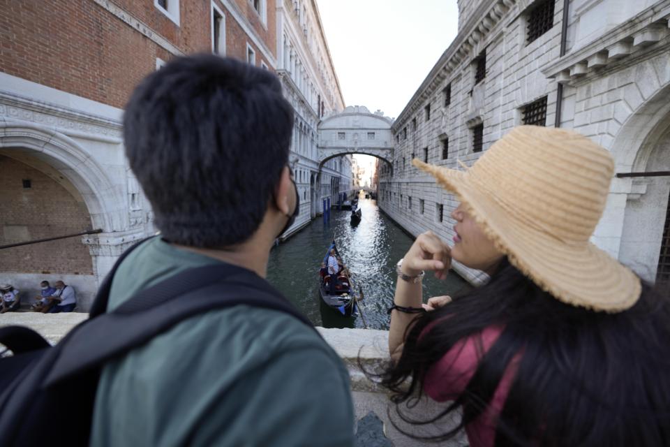 A couple admires the Ponte dei Sospiri (Bridge of Sighs), in Venice, Italy, Thursday, June 17, 2021. After a 15-month pause in mass international travel, Venetians are contemplating how to welcome visitors back to the picture-postcard canals and Byzantine backdrops without suffering the indignities of crowds clogging its narrow alleyways, day-trippers perched on stoops to imbibe a panino and hordes of selfie-takers straining for a spot on the Rialto Bridge or in front of St. Mark’s Basilica. (AP Photo/Luca Bruno)