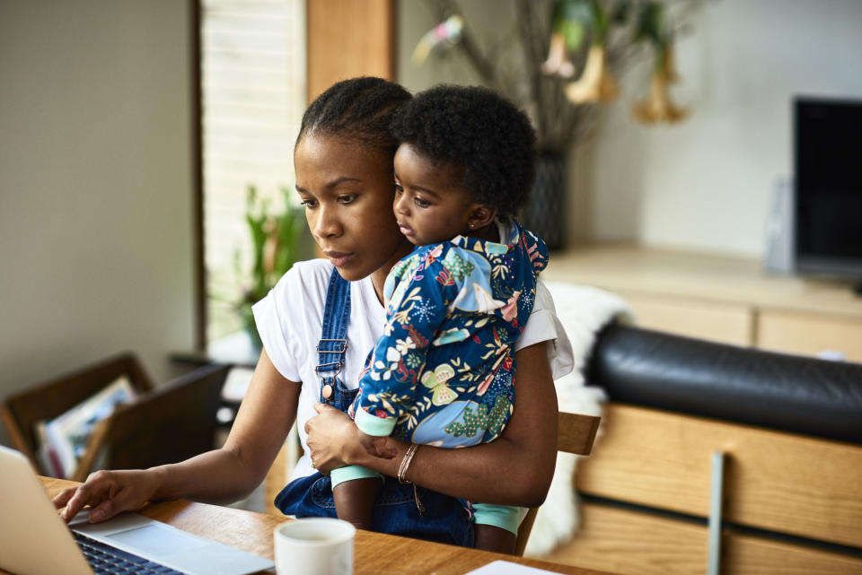 Woman working on laptop with child in a back carrier, displaying work-life balance