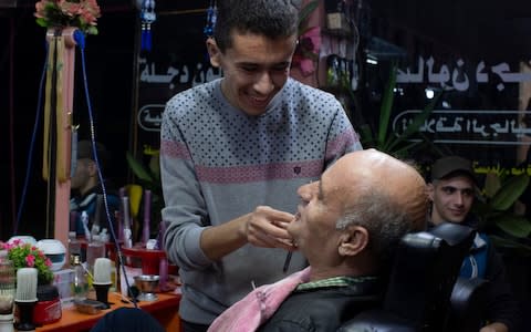 Mahmoud Mohammad Serhan, 59, a a retired trader who now keeps a farm, gets a cutthroat shave at a barber shop in Qamishli - Credit:  Sam Tarling