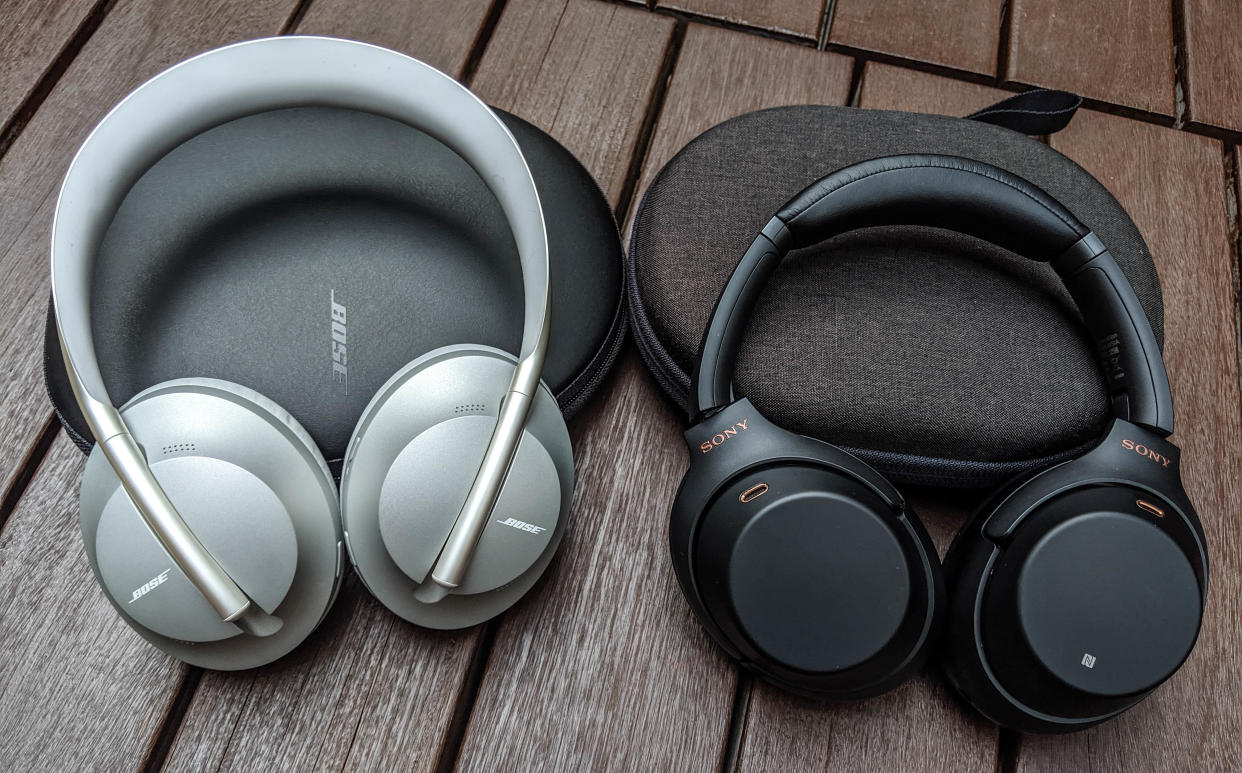  Bose silver over-ear headphones in silver and Sony black over-ear headphones on a wooden table 