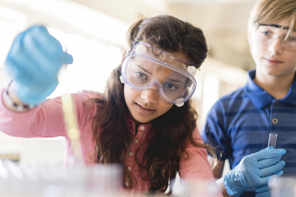 Two students in lab gear conduct an experiment with test tubes