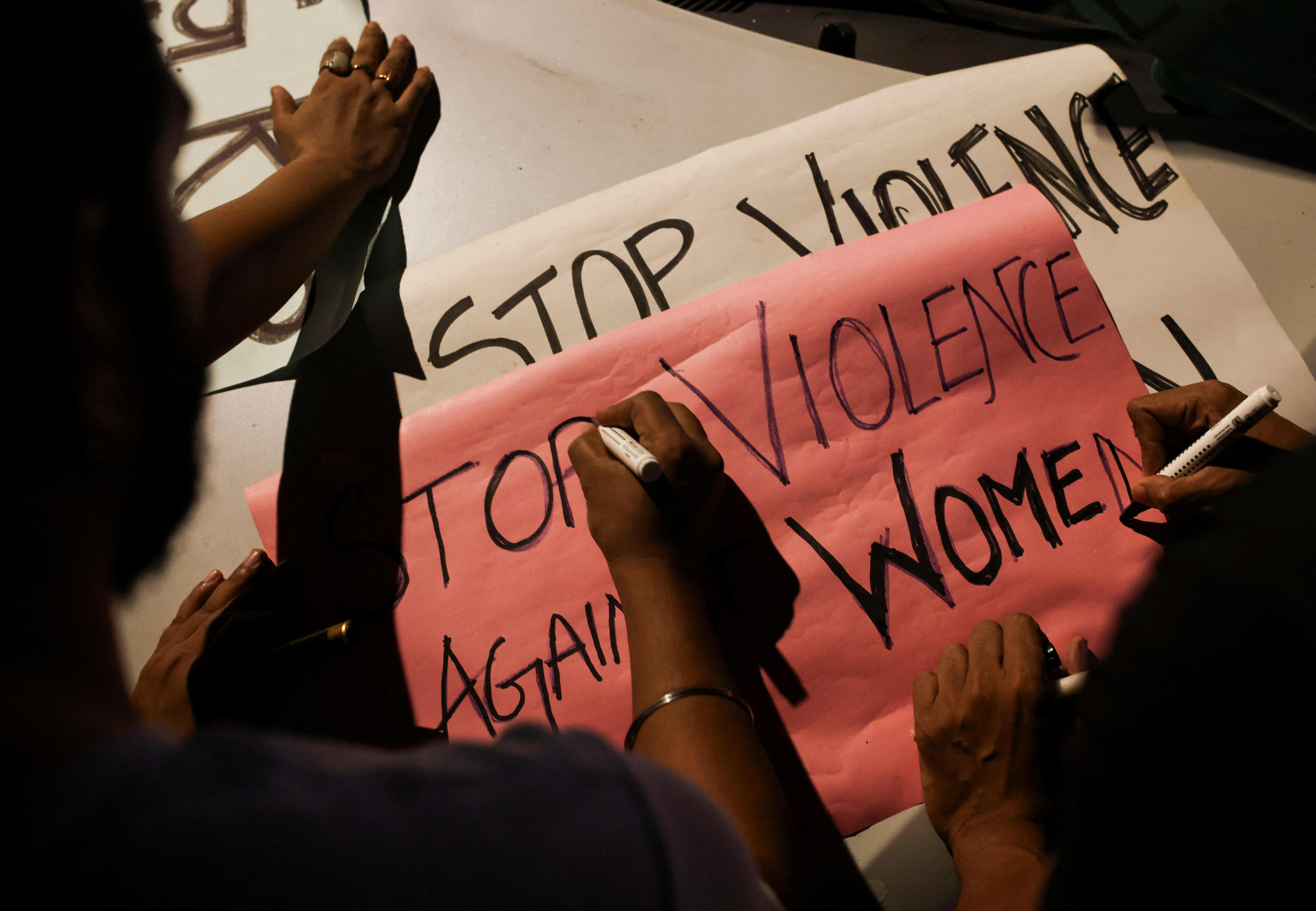 People write slogans on posters before the start of a candlelight vigil on Wednesday condemning the rape and killing of a trainee doctor.