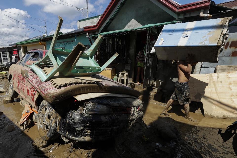 A man carries a cabinet past a broken car at the typhoon-damaged Kasiglahan village in Rodriguez, Rizal province, Philippines on Friday, Nov. 13, 2020. Thick mud and debris coated many villages around the Philippine capital Friday after Typhoon Vamco caused extensive flooding that sent residents fleeing to their roofs and killing dozens of people. (AP Photo/Aaron Favila)