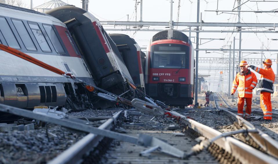 Rescue workers stand next to a derailed train after two trains collided near Rafz