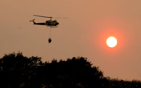 A helicopter carrying a load of water to tackle wildfires in California - Credit: AP