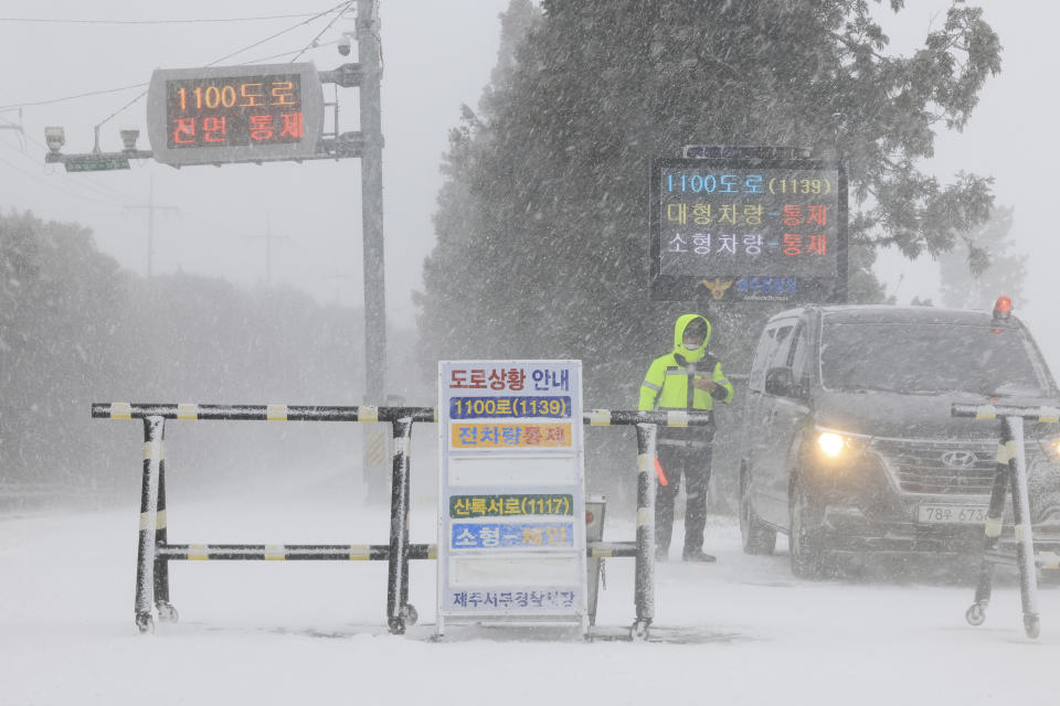 A police officer controls the entry of vehicles at a road amid heavy snowfall on Jeju Island, South Korea, Tuesday, Jan. 24, 2023. Thousands of travelers swarmed a small airport in South Korea's Jeju island on Wednesday in a scramble to get on flights following delays by snowstorms as frigid winter weather gripped East Asia for the second straight day. (Park Ji-ho/Yonhap via AP)