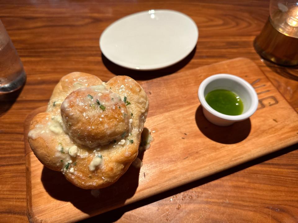 Garlic bread with herbs and a white sauce with a green dipping sauce off to the side and a white plate in the background