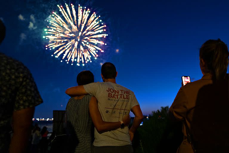 La gente observa cómo los fuegos artificiales estallan sobre el puerto de Nueva York para celebrar el fin de las restricciones