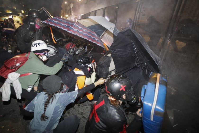 Demonstrators shield themselves with umbrellas as federal officers launch tear gas outside the Mark O. Hatfield United States Courthouse during a Black Lives Matter protest Friday, July 24, 2020, in Portland, Ore. (AP Photo/Marcio Jose Sanchez)