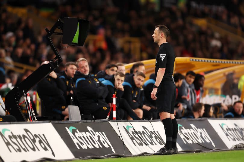 Stuart Attwell checks the VAR monitor before disallowing the goal scored by Hwang Hee-Chan of Wolverhampton Wanderers (not pictured) following a foul in the build up by Matheus Cunha of Wolverhampton Wanderers during the Premier League match between Wolverhampton Wanderers and AFC Bournemouth at Molineux on April 24, 2024 in Wolverhampton, England.