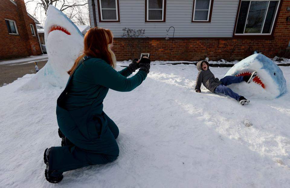 Jennifer Ramirez, of Madison Heights, photographs Colton Roberts, 5, of Madison Heights, in front of her great white snow sculpture on her front lawn Tuesday, Jan. 31, 2023. Ramirez, an art teacher, said it took her four to five hours on Saturday to gather and sculpt out of the snow two great whites and this fin.