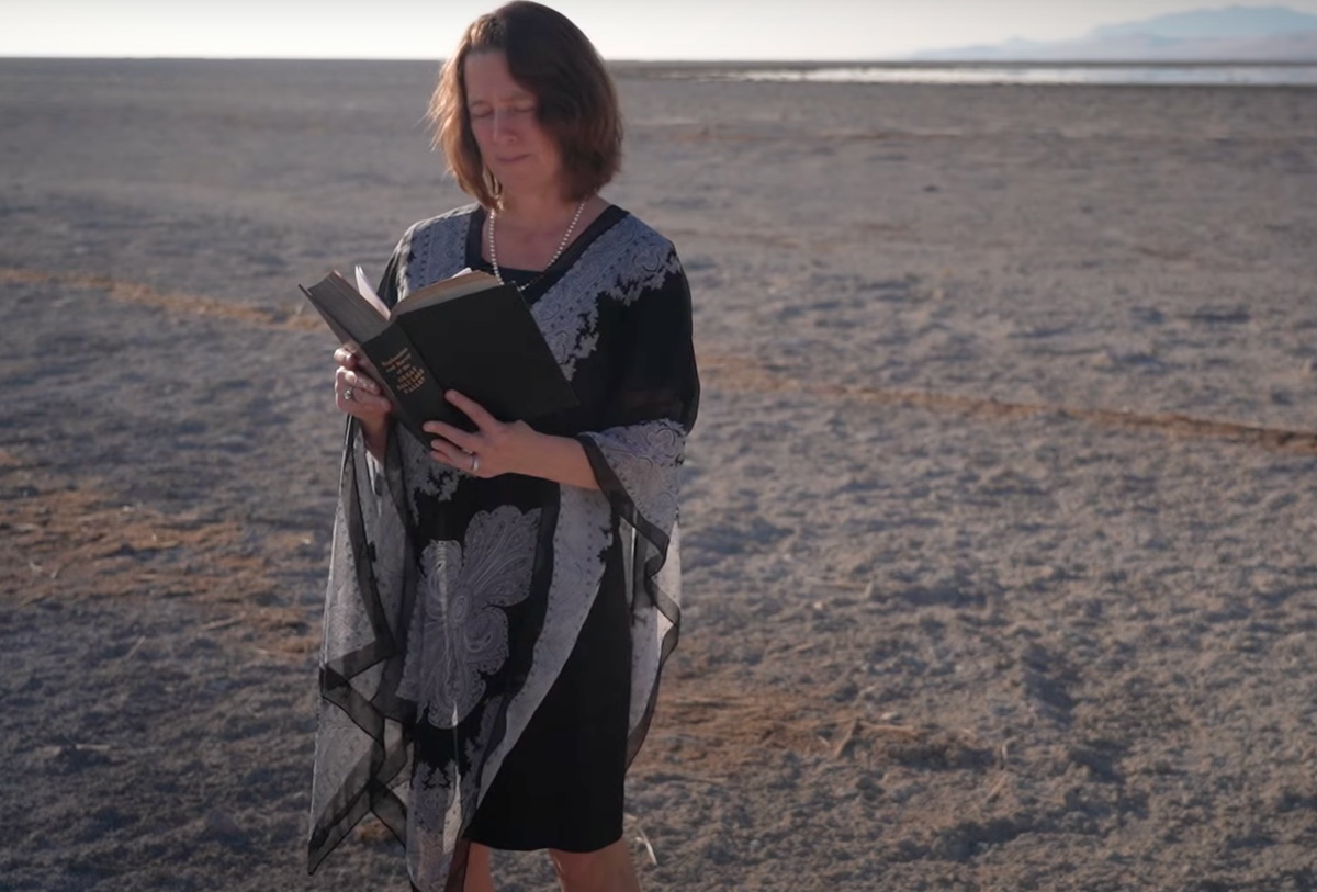 Bonnie Baxter reads an obituary standing on the dry ground where the Great Salt Lake has receded to raise awareness of its plight (Bonnie Baxter/The Salt Lake Tribune)