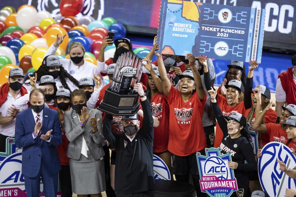 North Carolina State Head Coach Wes Moore holds up the championship trophy as his team celebrates their victory over Louisville in the championship of the Atlantic Coast Conference NCAA women's college basketball game in Greensboro, N.C., Sunday, March 7, 2021. (AP Photo/Ben McKeown)