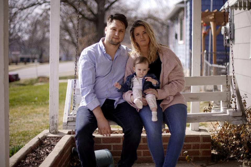 Logan DeWitt with his wife Mckenzie and daughter Elizabeth sit on the front porch of their home Monday, March 8, 2021, in Kansas City, Kan. Because he could work at home, Logan kept his job through the pandemic while his wife lost hers and went back to school. Their financial situation was further complicated with the birth of their daughter nine months ago. (AP Photo/Charlie Riedel)