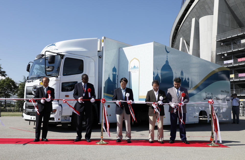 In this July 23, 2018, photo provided by Mobile Mosque Executive Committee, guests cut a ribbon during an unveiling event for Mobile Mosque, a mosque on wheels with the capacity for up to 50 people at Toyota Stadium in Toyota, western Japan. As Japan prepares to host visitors from around the world for the Summer Olympics in 2020, a Tokyo sports and cultural events company has created a mosque on wheels that its head hopes will make Muslim visitors feel at home. (Mobile Mosque Executive Committee via AP)