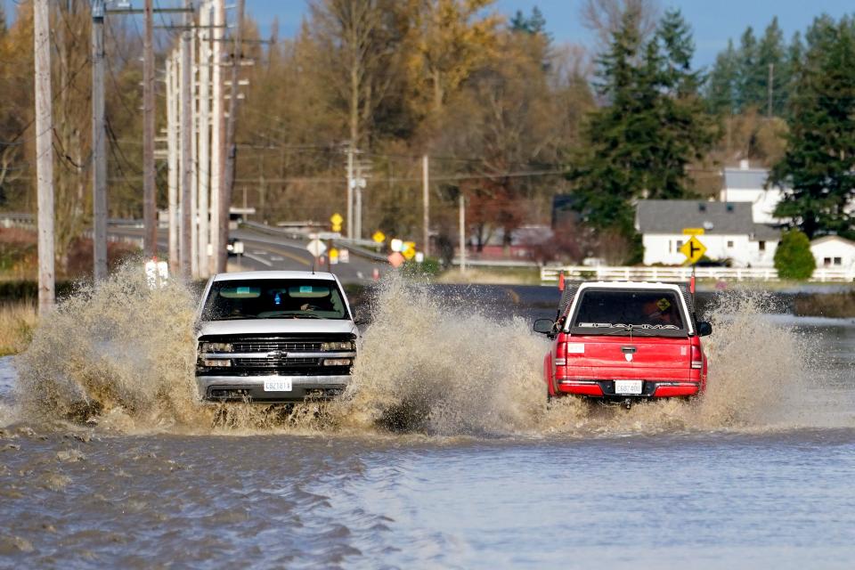 Pickup trucks send up plumes of muddy water as they pass on a flooded road, Tuesday, Nov. 16, 2021, near Everson, Wash.