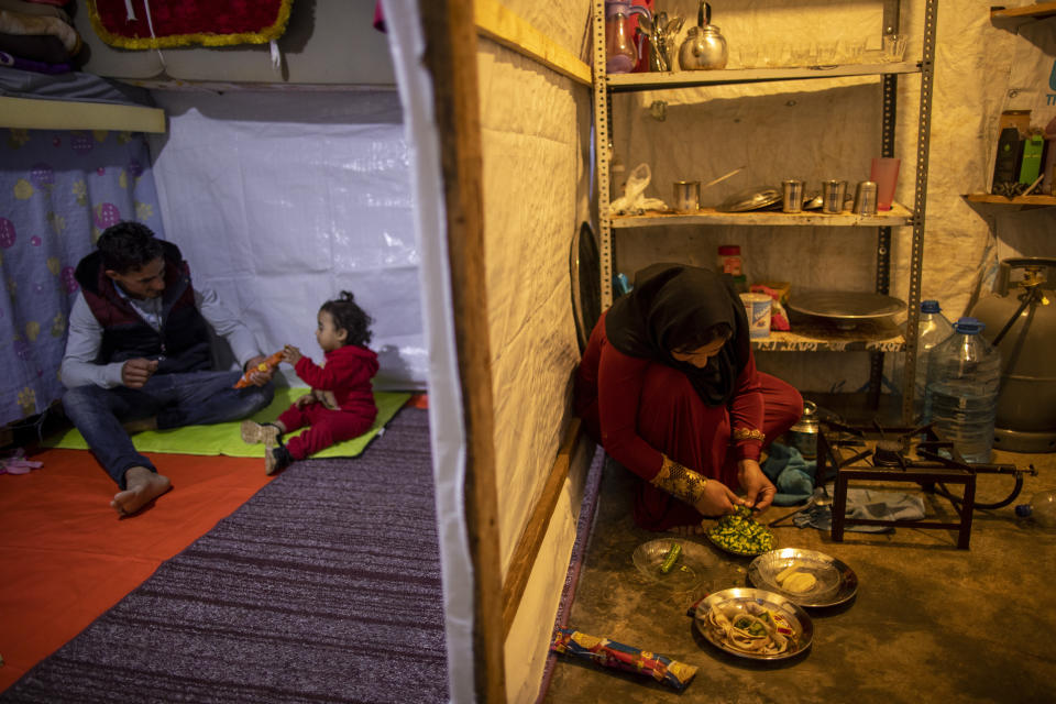 Syrian refugee Ayesha al-Abed, 21, right, prepares food as her Husband Raed Mattar, 24, left, plays with their daughter Rayan, 18 months old, before they break their fast on the first day of fasting month of Ramadan, at an informal refugee camp, in the town of Bhannine in the northern city of Tripoli, Lebanon, Tuesday, April 13, 2021. (AP Photo/Hassan Ammar)