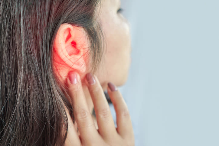 Close-up of a person with an ear infection, indicated by a red, inflamed ear, and the person touching their ear