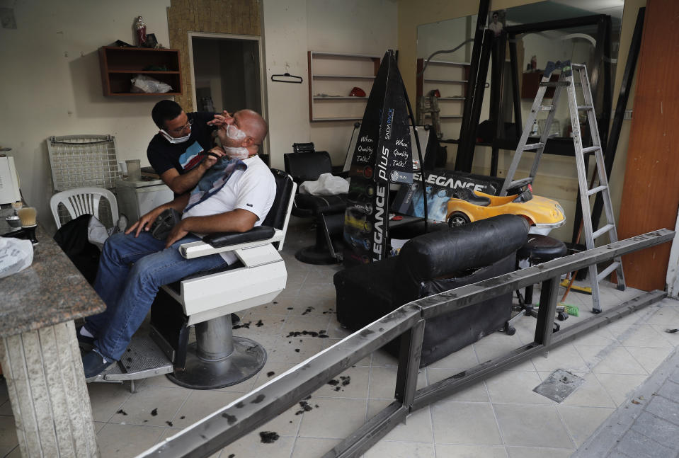 A Lebanese barber shaves the beard of a customer, at a men salon that damaged by last week's explosion that hit the seaport of Beirut, in the middle of a damaged street at Mar Mikhael neighborhood, in Beirut, Lebanon, Friday, Aug. 14, 2020. (AP Photo/Hussein Malla)