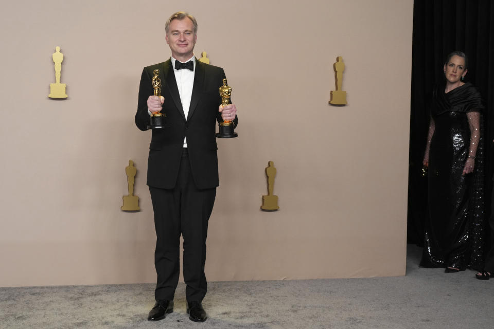 Christopher Nolan poses in the press room with the awards for best director and best picture for "Oppenheimer" at the Oscars on Sunday, March 10, 2024, at the Dolby Theatre in Los Angeles. Emma Thomas, winner of the award for best picture for "Oppenheimer," looks on from the right. (Photo by Jordan Strauss/Invision/AP)