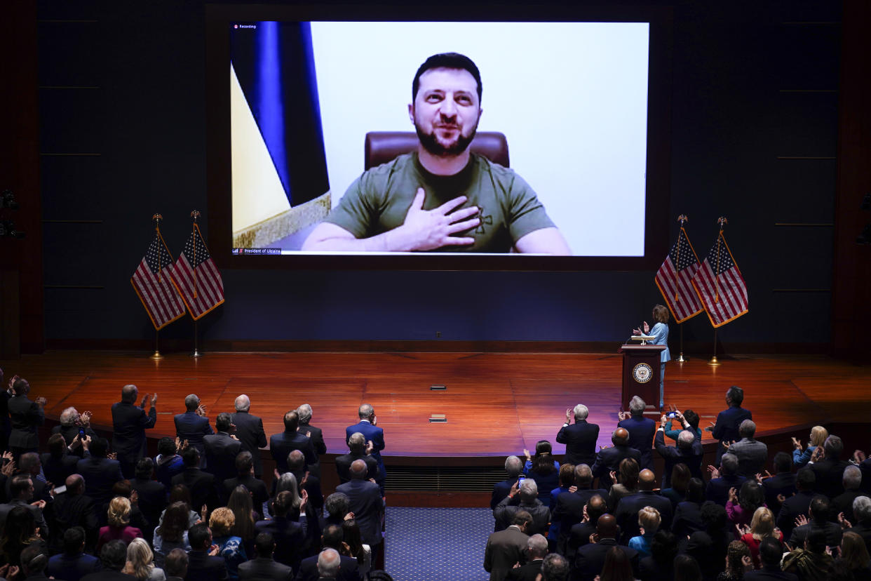 Large screen behind a stage before Congress shows Volodymyr Zelensky, with Nancy Pelosi standing onstage at a podium.