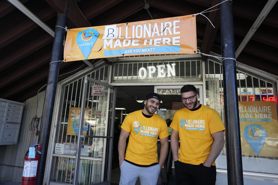 Chris Khalil, left, and Jonathan Khalil, sons of the store co-owners, stand beneath a banner put up by lottery officials outside the Midway Market & Liquor where a winning ticket was sold in Frazier Park, Calif., Thursday, Oct. 12, 2023. The liquor store in a tiny California mountain town reverberated with excitement after word that the winning ticket for a $1.765 billion Powerball jackpot was sold there. The drawing Wednesday night ended a long stretch without a winner of the top prize. (AP Photo/Marcio Jose Sanchez)