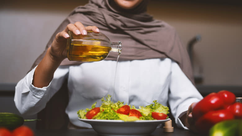 person drizzling oil on salad