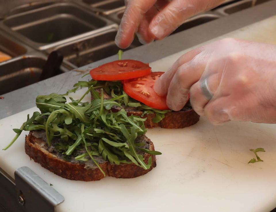 Sam LaVictoire, former owner of NOMZ, prepares a signature avocado black bean sandwich as he helps train the eatery's new owners.