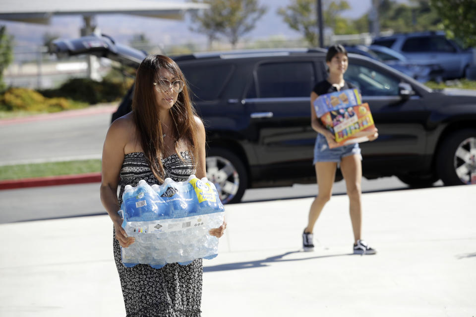 Christine Price, left, drops off food and water for evacuees from the Tick Fire with the help of her daughter Tinley, background right, at a shelter at West Ranch High School Friday, Oct. 25, 2019, in Santa Clarita, Calif. (AP Photo/Marcio Jose Sanchez)