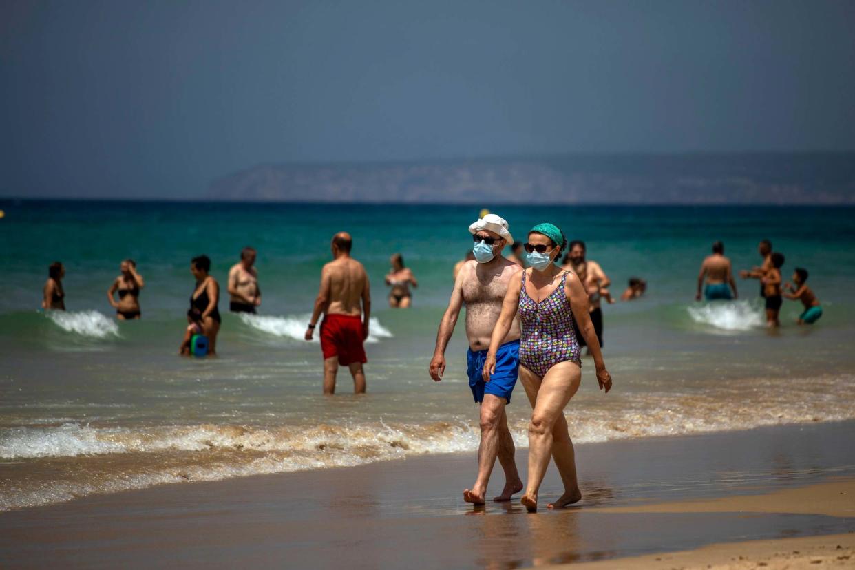 A couple wearing face masks walk along the shore in a beach in Cadiz, south of Spain, on Tuesday, July 21, 2020: AP