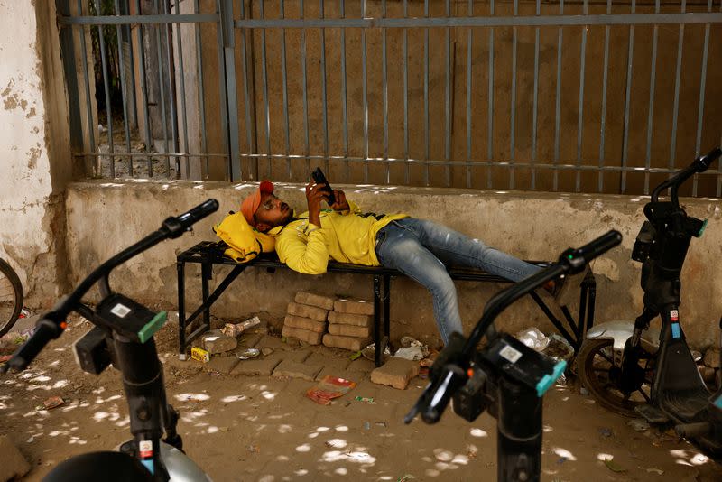 Delivery partner with Blinkit, an Indian online-delivery company, rests on a bench near one of the company's dark stores on a hot summer day during a heatwave in New Delhi