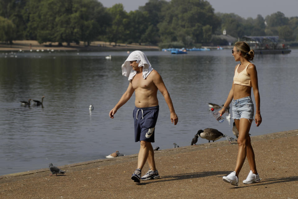 FILE - In this Wednesday, Aug. 12, 2020 file photo, a man keeps cool with a shirt over his head as he walks alongside The Serpentine in Hyde Park in London with high temperatures forecast again for many parts of England. (AP Photo/Kirsty Wigglesworth)