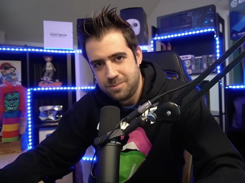 Genes sitting in front of a microphone, in a room decorated with blue twinkly lights.