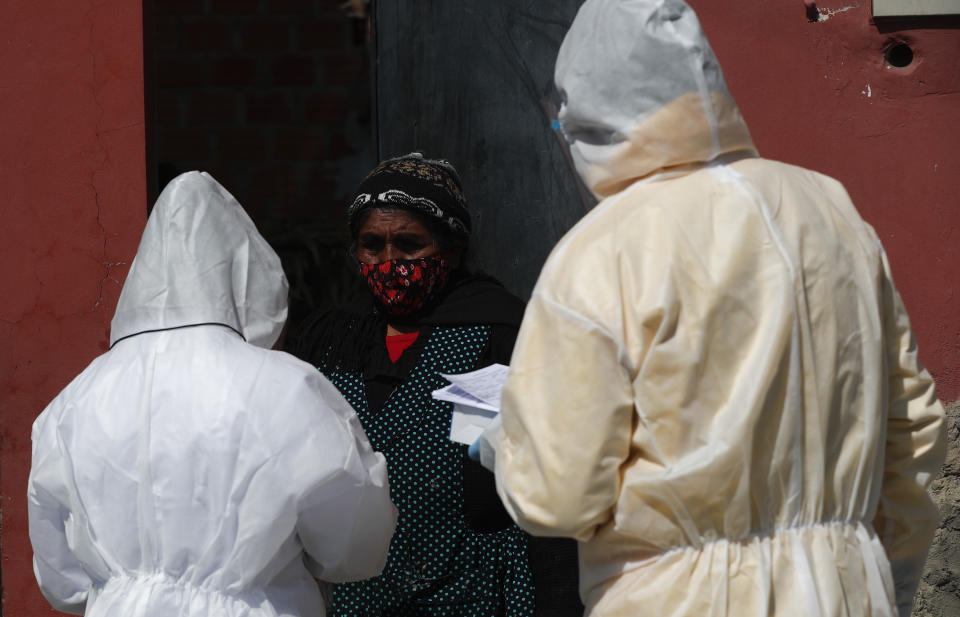 Healthcare workers dressed in full protective gear interview a resident during a house-to-house campaign against the spread of the new coronavirus, in the Mallasa neighborhood of La Paz, Bolivia, Saturday, Aug. 8, 2020. (AP Photo/Juan Karita)