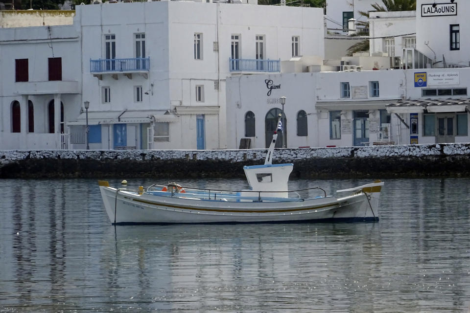In this Tuesday, June 9, 2020, photo, a fishing boat is anchored in front of the main walkway on the Greek island of Mykonos, Greece. Business owners and locals officials on the Greek holiday island of Mykonos, a popular vacation spot for celebrities, club-goers, and high rollers, say they are keen to reopen for business despite the risks of COVID-19 posed by international travel. Greece will officially launch its tourism season Monday, June 15, 2020 after keeping the country's infection rate low. (AP Photo/Derek Gatopoulos)