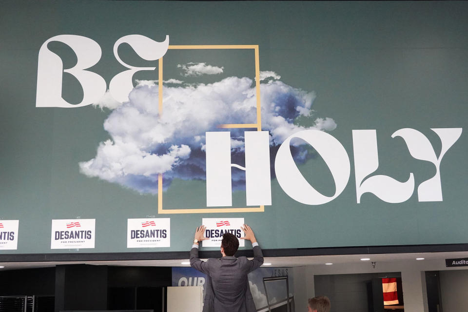 A worker puts up DeSantis for President stickers under a sign that reads. 