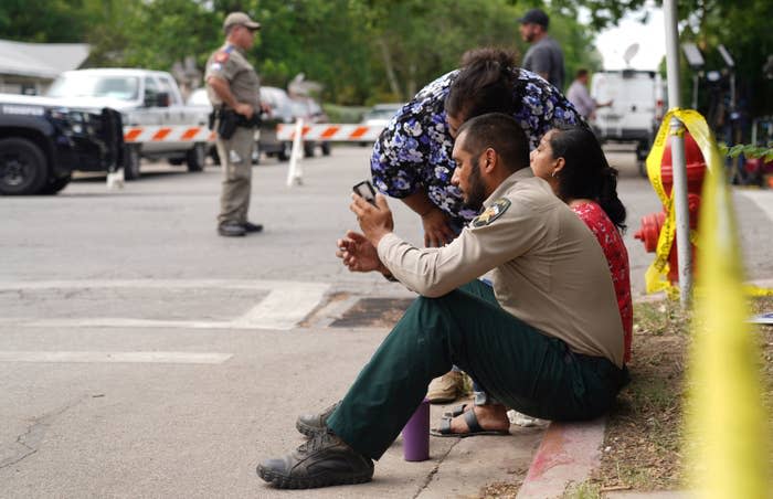 Deputy Sheriff Felix Rubio, who lost his daughter, Alexandria Rubio, 10, in the mass shooting, checks his phone as he sits by his wife, Kimberly, center, on the sidewalk outside Robb Elementary School while state troopers monitor the area in Uvalde, Texas, on May 24, 2022.