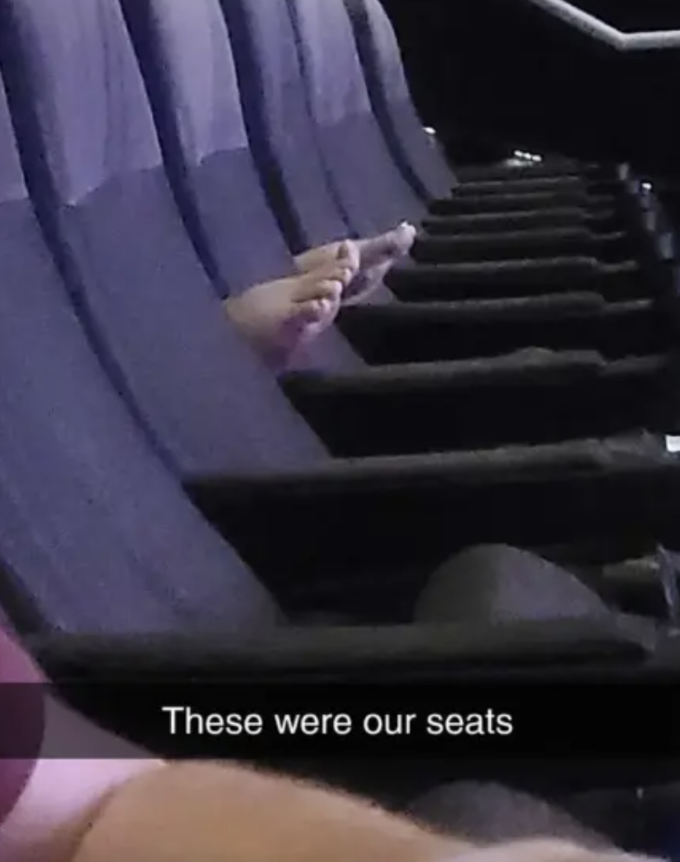 Photo of several empty theater seats with a person's hand indicating their assigned seating area; text overlay "These were our seats"