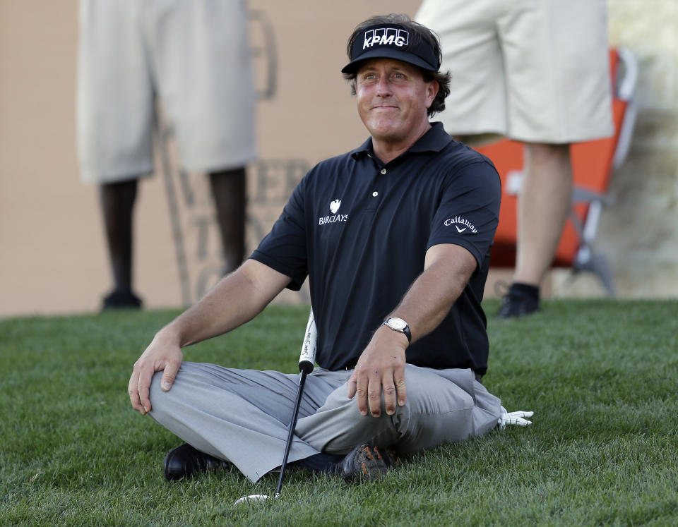 Phil Mickelson sits on the grass as watches his playing partners finish the 16th hole during the second round of the Texas Open golf tournament, Friday, March 28, 2014, in San Antonio. (AP Photo/Eric Gay)